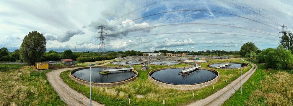 Aerial view of the Thames Water Sewage Works featuring circular sedimentation tanks, surrounding green fields, and overhead power lines in Hoddesdon, England, United Kingdom.