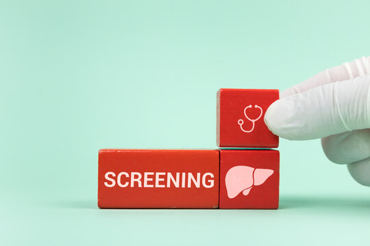 Concept of early detection of liver disease and liver health awareness. A doctor's hand places wooden cubes with icons of the liver and gallbladder. Green background.