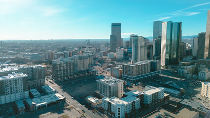 Fototapeta premium Vast, lowrise commercial zones sit prominently beneath looming silhouette of downtown financial core. Long, distinct shadows emphasize expansive grid patterns found throughout Denver, CO