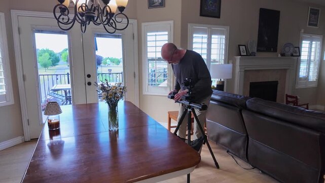 A senior man setting up a motorized camera slider on a tripod in a living room for a video production