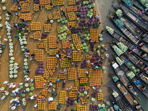 Sylhet, Bangladesh - 07 February 2026: Aerial view of a vibrant floating market with farmers and traders sorting colorful piles of fresh vegetables beside traditional wooden boats.
