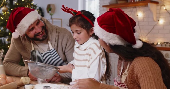 Christmas family baking cookies in home kitchen. Parents and child sift flour together with sieve, make dough for festive shapes cutting, dessert preparation by happy father, mother and child