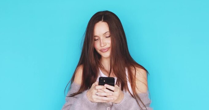 Young woman looking at smartphone screen with calm pensive facial expression, brunette girl browsing mobile phone with serious relaxed look, studio isolated on blue background, tech use, contemplation