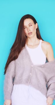 Skeptical young woman rolling her eyes with annoyed face, showing boredom and making funny silly grimace with closed eyes, looking indifferent and unsatisfied against vibrant blue background