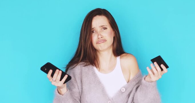 Confused young woman facing online payment failure with credit card and smartphone, showing disappointed expression and shrugging shoulders in doubt, looking upset isolated on blue background