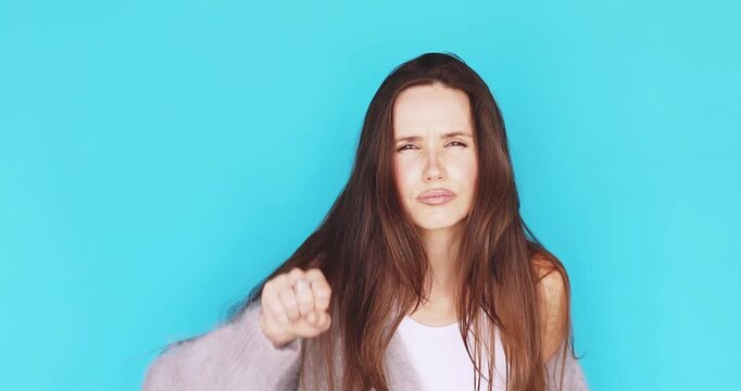 Skeptical young woman squinting and peering closely, knocking on invisible glass with fist to check or ask who is there with distrustful facial expression isolated on vibrant blue studio background