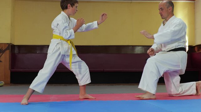 A coach and a little athlete perform a stand-up jump from a sitting position
