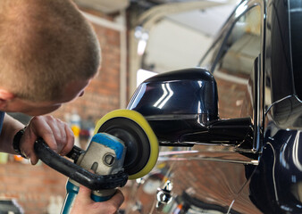 Fototapeta premium Man polishes the glass of a car headlight with a polishing machine from small scratches, chips. Process polishing of the front car headlights. Hands of male professional worker with orbital polisher. 