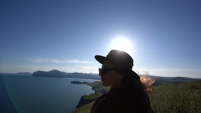 Woman hat summer, happy woman wearing fedora hat and sunglasses standing on grassy cliff overlooking scenic blue ocean bay during sunny day