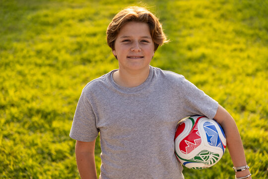 portrait of pre teen boy holding soccer ball on green lawn with net in background