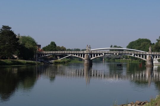 Elegant suspension bridge spans calm river on sunny day.