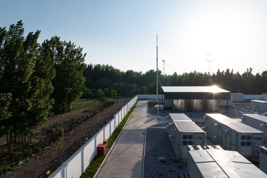 Outdoor telecommunications base station equipment array with perimeter fence and tree belt in early morning sunlight