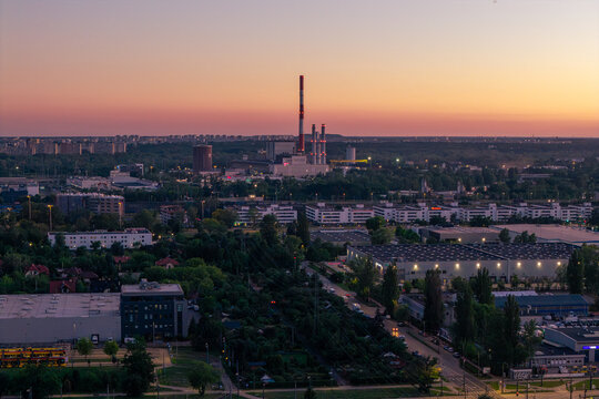 Warszawa, Poland - 23 June 2026: Aerial view of EC Siekierki power plant, featuring its tall chimney and industrial structures amidst urban greenery and residential buildings at sunset.