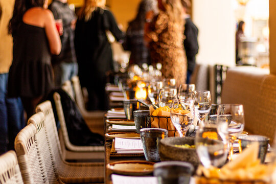 Restaurant dining table prepared for guests with elegant table settings, candlelight, wine glasses, and people socializing in the background