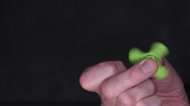 Close-up of a hand spinning a green fidget spinner, showcasing the continuous motion and design details, with a dark background enhancing the vibrant color and movement of the toy