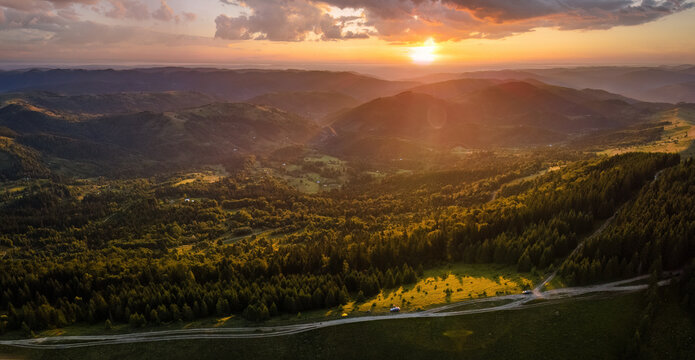 Amazing mountain landscape. Bright colorful sunset in wild national park highlands. Dark dirt road winding on hilltop illuminated with yellow setting sun