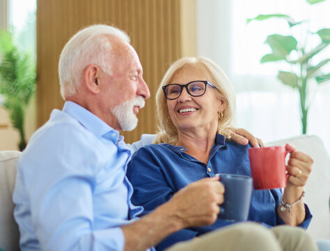 Portrait of a happy senior couple embracing talking and drinking coffee or tea at home