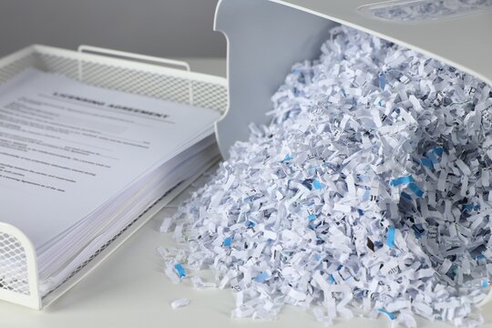 Shredder with cut paper pieces and documents on white table, closeup