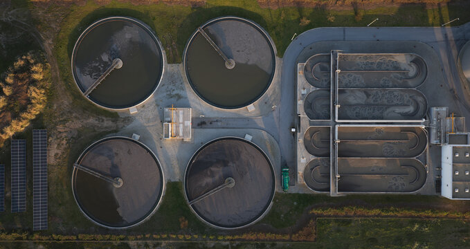 Portugal - 25 June 2026: Aerial view of a water treatment plant at sunset, featuring circular sedimentation tanks, rectangular aeration basins, and rows of solar panels.