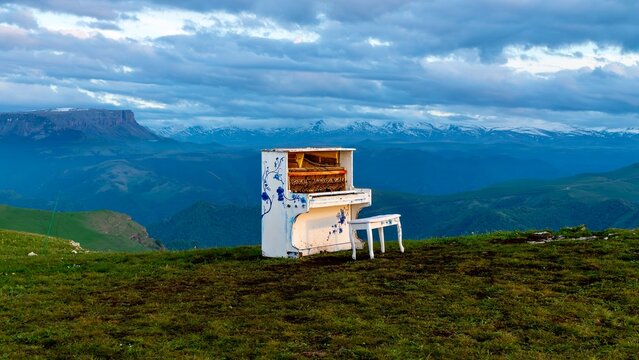 Dzhily Su, Russia - June 4, 2026: Old piano standing outdoors with mountains in the background, creating an unusual scene with a weathered instrument, highland landscape, green hills, and scenic Cauca