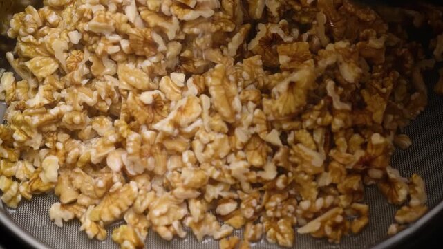 High-angle macro shot of a heap of peeled, golden-brown walnut kernels being prepared as a topping or ingredient for a homemade dessert pie. The footage highlights the natural texture and organic qual