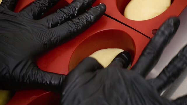 Close-up of a baker using black nitrile gloves to carefully prepare individual dessert pies or tarts in a professional kitchen. The use of specialized silicone molds ensures consistent shape for gourm