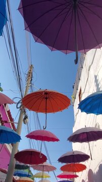 Low angle view of vibrant multi colored umbrellas suspended between buildings in historic center against a clear blue sky in Cartagena Colombia