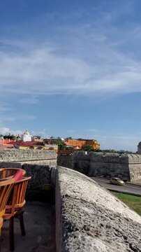 Beautiful view from the stone defensive walls showcasing empty restaurant tables a palm tree and the modern skyline of Cartagena Colombia