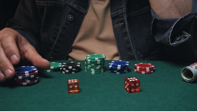 Male player places red dice on green felt poker table surrounded by stacks of colorful poker chips and a rolled-up card