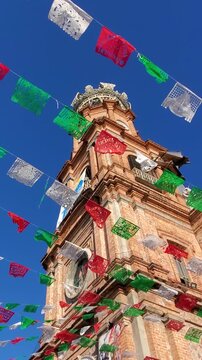 Looking up at the historic red brick tower of Our Lady of Guadalupe Church adorned with colorful flags in Puerto Vallarta Mexico