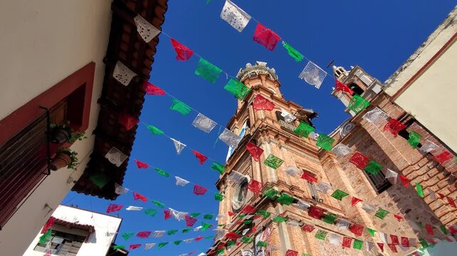 Looking up at the historic red brick tower of Our Lady of Guadalupe Church adorned with colorful flags in Puerto Vallarta Mexico