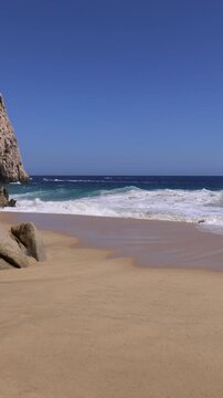 Scenic view of powerful ocean waves breaking on a golden sand beach next to dramatic rock cliffs in Cabo San Lucas Mexico at Los Arcos
