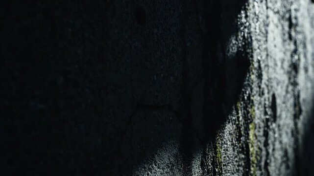 Closeup of textured dark surface with cracks and moss on a weathered wall