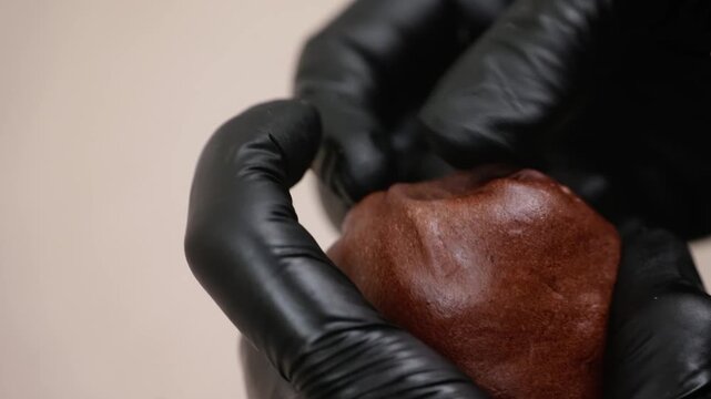 High-angle, macro shot of a confectioner wearing professional black nitrile gloves gently pressing a soft, warm chocolate-filled pastry or pie. The footage highlights the rich, glossy texture of the c
