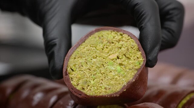 A gourmet cross-section shot of the trending Dubai Chewy Cookie, featuring a rich, green pistachio and crispy kataifi pastry center encased in a thin, dark cocoa chewy outer shell. The dessert is bein