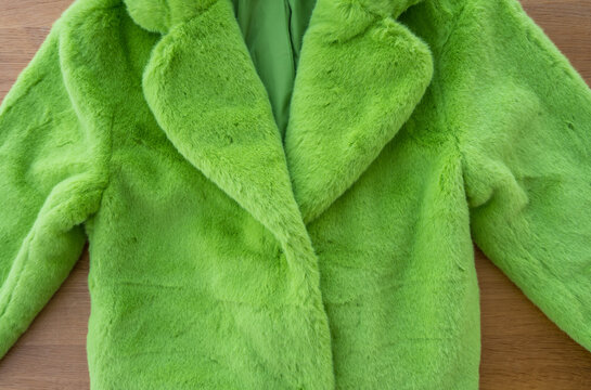 Top-down view of a vibrant green faux fur coat made of recycled polyester, spread out on a wooden surface. The plush texture and bold color highlight sustainable fashion, winter style