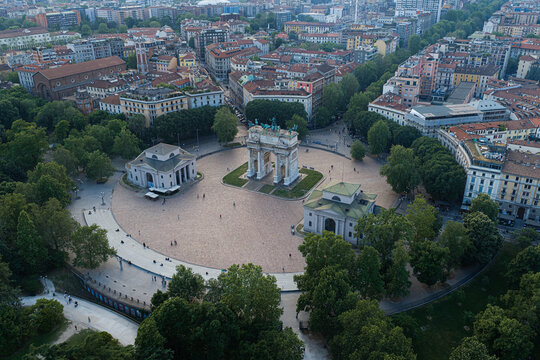 Aerial view of Arco della Pace in Parco Sempione, surrounded by lush trees, historic buildings, and urban streets in Milan, Lombardy, Italy.