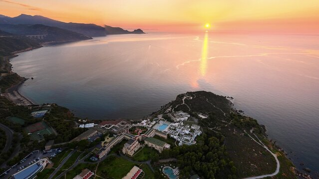 Aerial view of a coastal resort in Pollina at sunset, featuring swimming pools, lush greenery, and a scenic coastline overlooking the Tyrrhenian Sea in Pollina, Sicilia, Italy.