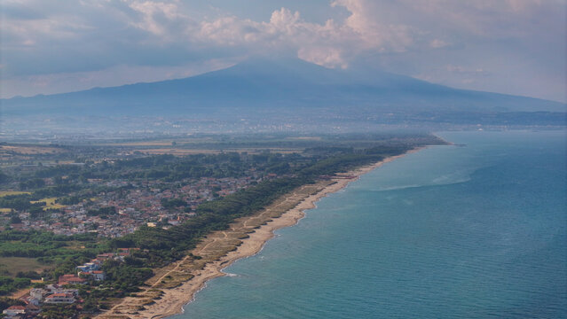 Aerial view of the coastline near Brucoli featuring sandy beaches, lush greenery, and the imposing Mount Etna volcano in the background in Brucoli, Sicily, Italy.