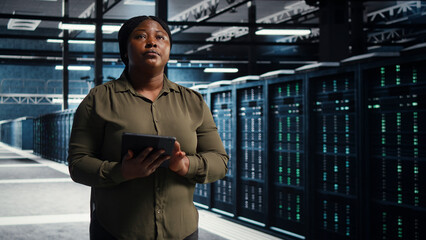 Fototapeta premium Data center engineer walks through a server room while overseeing IT infrastructure and network operations.