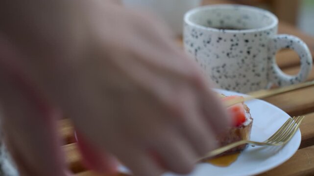 Hand sets plate with toast, strawberries, fork and knife on table beside mug. Concept of breakfast serving and morning routine