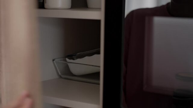 Woman opens kitchen cabinet and reaches for glass jar of honey on shelf. Concept of home cooking and pantry storage