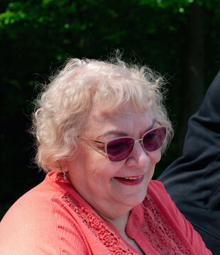 Close up portrait of a senior blonde woman wearing pink sunglasses and a coral lace blouse