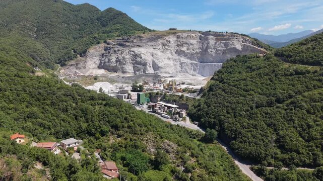 Aerial view of an open pit limestone quarry with massive terraced rock faces and an active processing plant surrounded by forested hills near Salerno, Italy