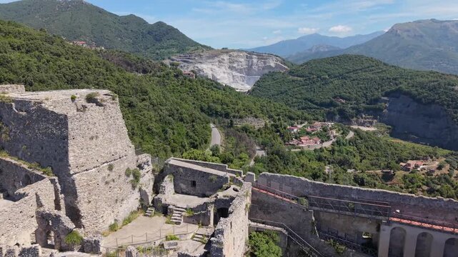 Aerial view of Castello di Arechi medieval stone ruins and ramparts surrounded by lush mountain valley, forest, village, and limestone quarry, Salerno, Italy