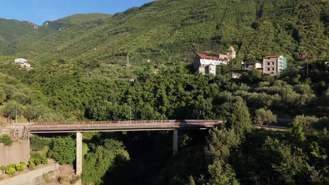 Aerial view of modern road viaduct spanning lush green valley with Parrocchia Sant'Agnello Abate church, bell tower and buildings on hillside in Gragnano, Naples, Italy

