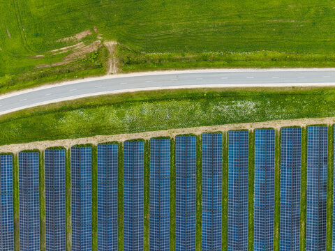 Aerial view of a solar farm with rows of photovoltaic panels set in a green field next to a road in Suntazi, Ogre Municipality, Latvia.