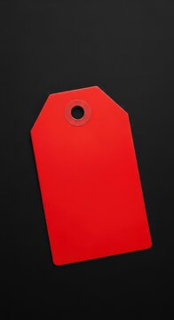 A vibrant red blank retail price tag, commonly used for sales and discounts, lies flat against a very dark, black background creating strong visual contrast, surface, abstract, affordability