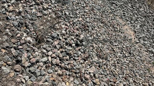 Rubble riverbank covered with stainless mesh, chain link overlay on coarse gravel and crushed stone, no people present, industrial