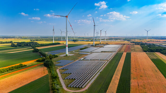 Turbines and solar panels. Wind turbines turn in the breeze while solar panels collect sunlight in a large field at midday.